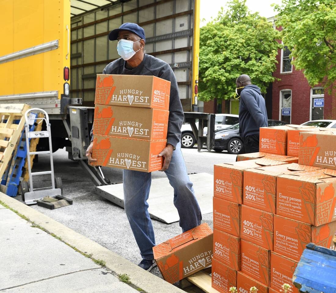 A person wearing a face mask unloads boxes of produce from a truck