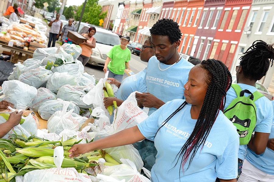 Wearing matching blue T-shirts, volunteers hand out food, including ears of corn