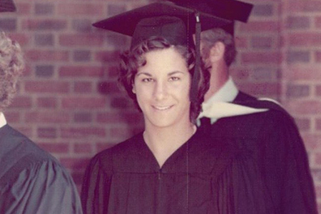 A young woman in a cap and gown looks into the camera