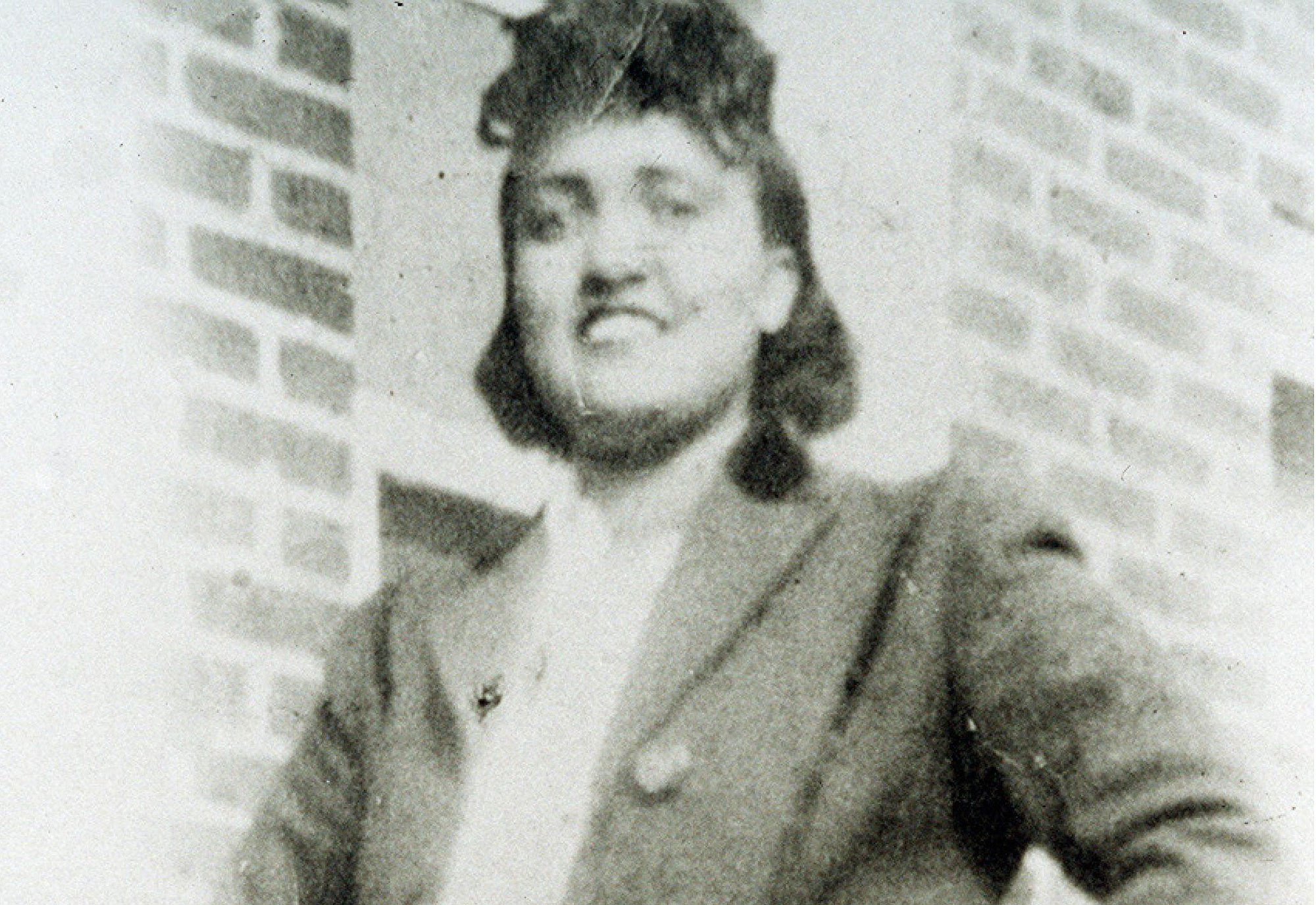 In this black and white photo, a woman stands smiling, her hands on her hips