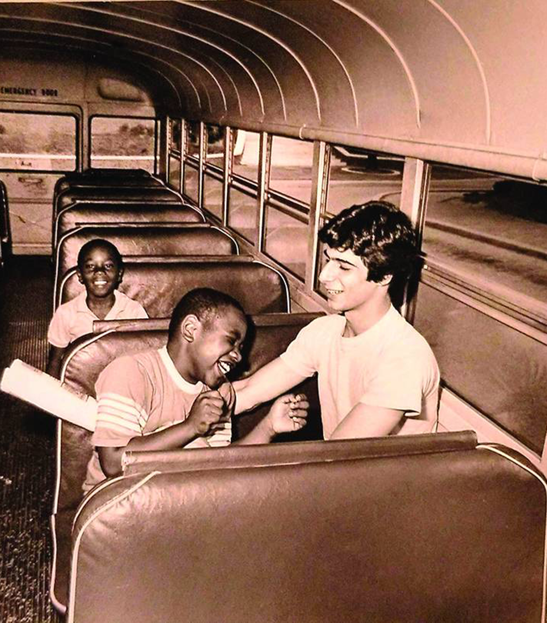A young adult sits on a bus with two smiling children